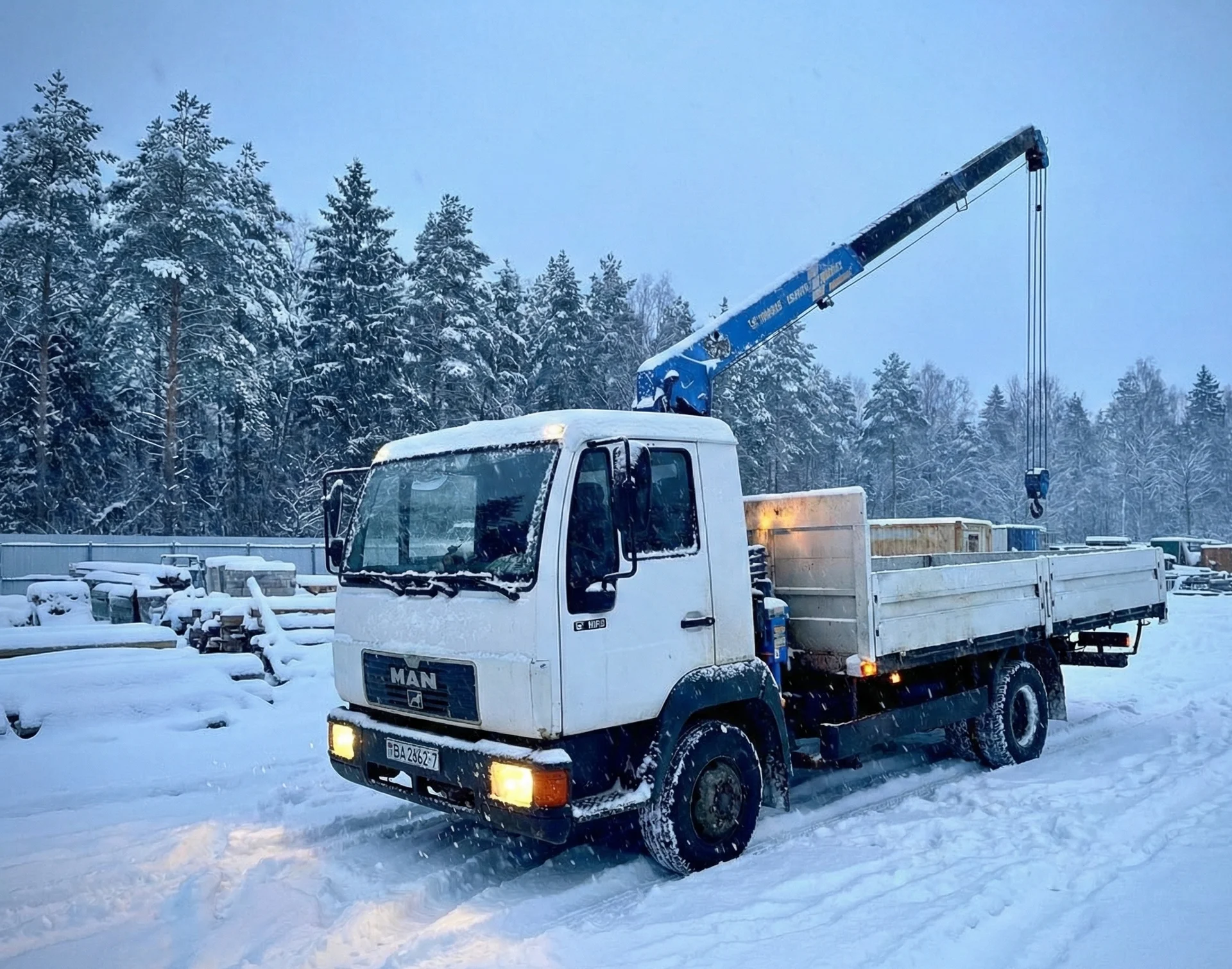 Кран-манипулятор поднимает бетонные кольца для установки колодца